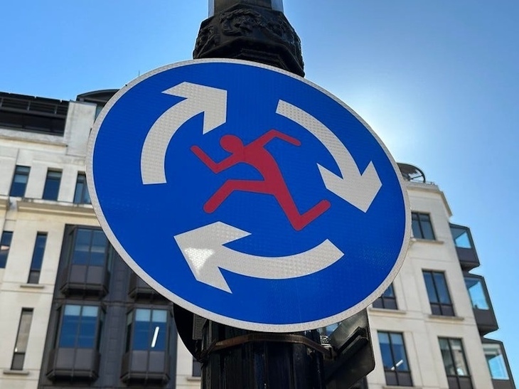 A roundabout sign with a running man in the middle