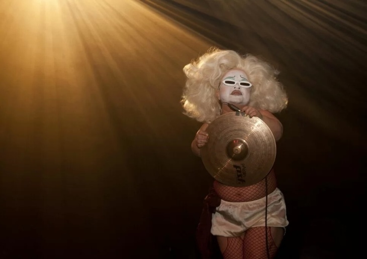 A person in a blonde wig and sunglasses clutching a cymbal