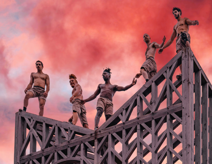 Free events in London: Five people standing atop a wooden frame, with a pink sky in the background