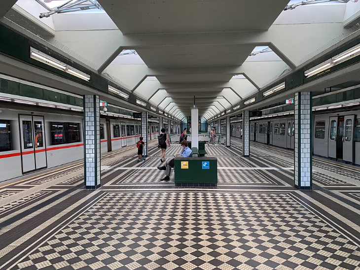 An island style platform in a U-Bahn station with a black and while chequerboard tiled floor