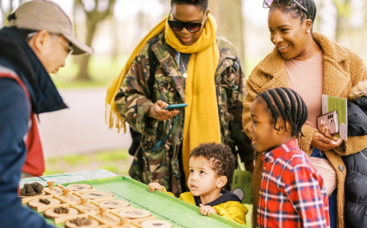 October half term 2025 events London: a staff member talking to two women and two young children in front of a table of specimens