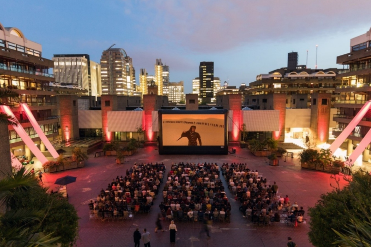 Things to do in London today: people in rows of seats watching a film on a large screen in an open-air courtyard at Barbican