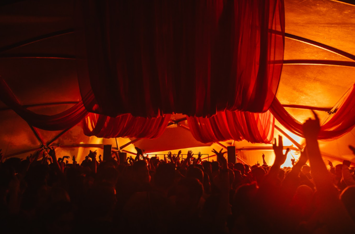 Things to do in London August bank holiday weekend: people raising their hands in a dimly lit crowd at a festival