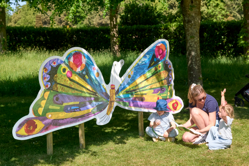 Things to do in London today:  a woman and two young children in front of a large illustration of a butterfly, in a garden