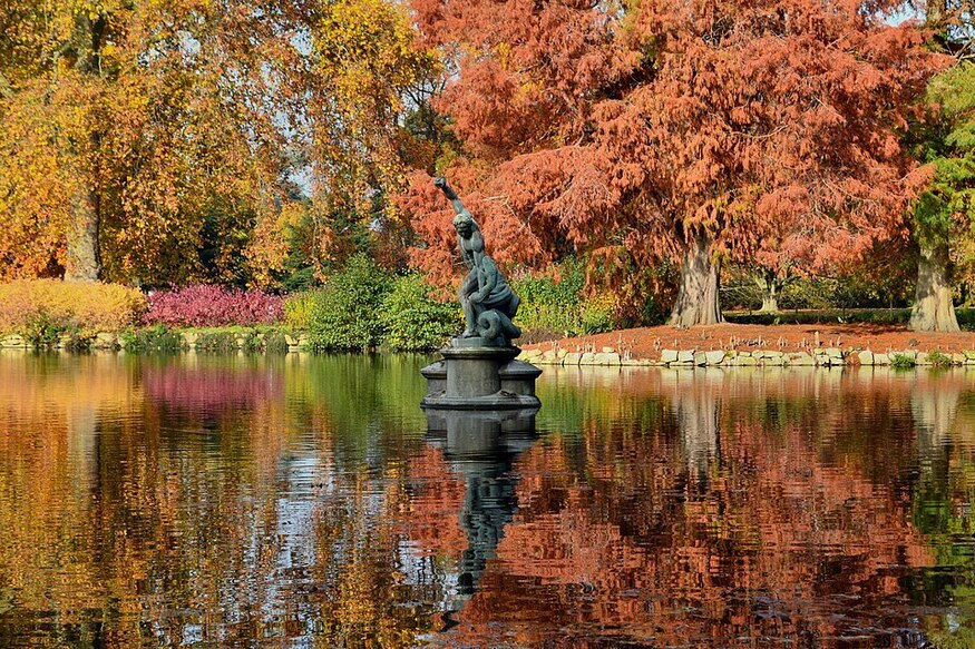 Autumn/fall walks in London: colourful leaves reflected in a lake, with a statue in the centre