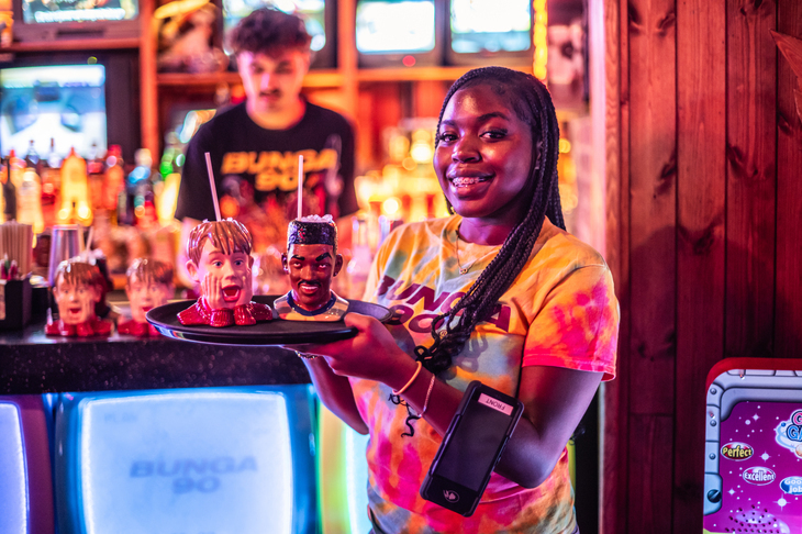 A waitress with cocktails in vessels resembling will smith and macaulay culkin