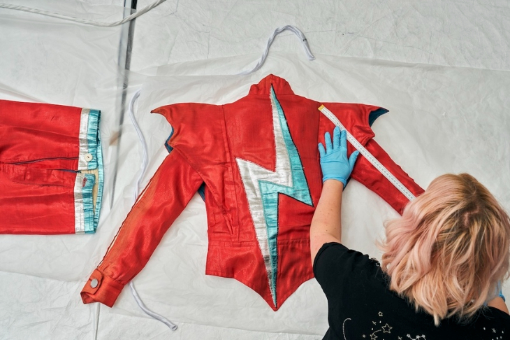 Things to do in London today: a curator laying out a red jacket with a lightning flash decoration