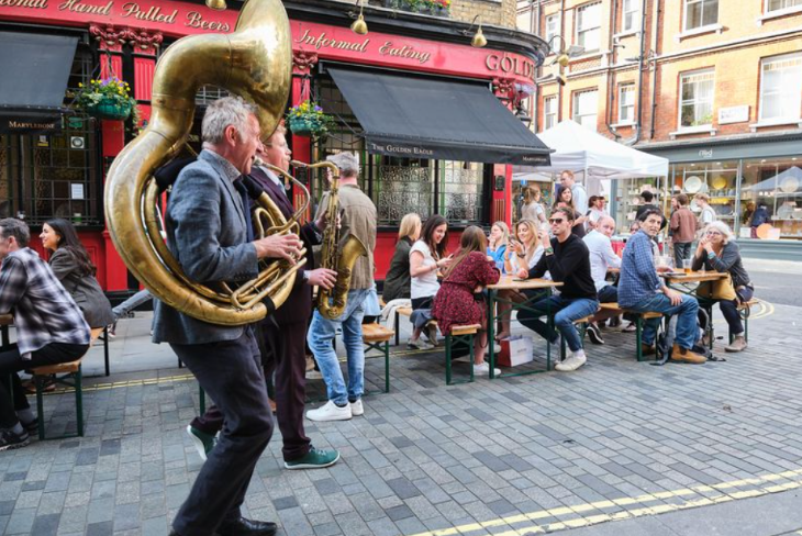 Things to do in London this weekend: a brass band walking down a street while people watch from pub benches nearby