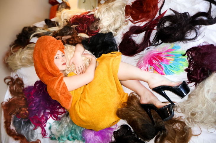 Things to do in London today: a woman with a towel wrapped around her lying on a bed surrounded by wigs