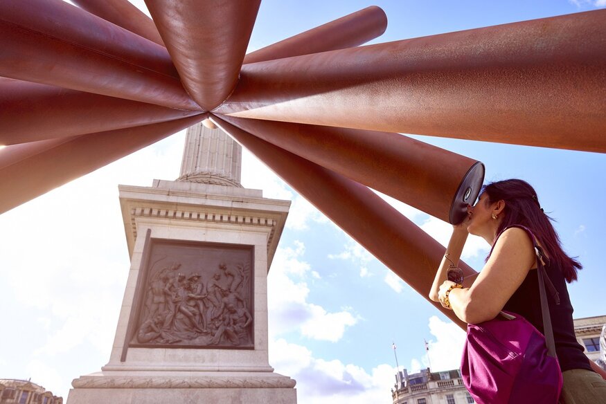 A woman looking through one of many telescopes at the bottom of Nelson's Column