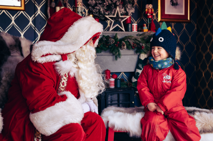 Hyde Park Winter Wonderland 2025: A young child sitting next to Santa in front of a fire place