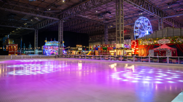 Christmas 2025 ice rinks London: a large indoor ice rink surrounded by funfair rides
 
