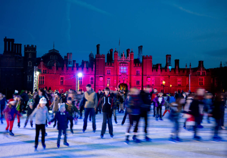 People skating on an ice rink in front of Hampton Court Palace, which is illuminated in pink