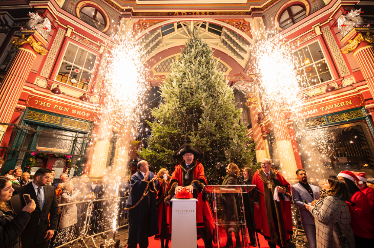 London Christmas lights 2025 switch-on dates: a former Lord MAyor pressing a button to light the Christmas tree at Leadenhall Market, surrounded by fireworks and a crowd