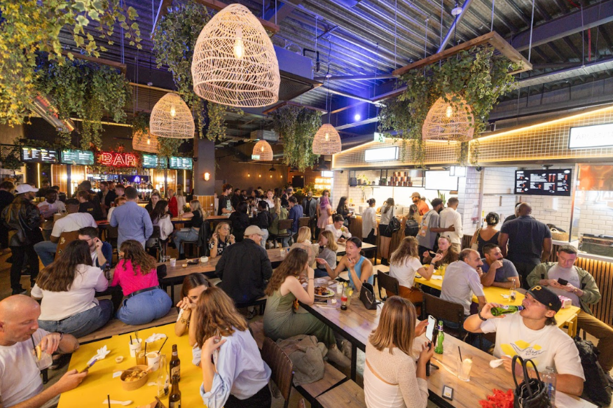 People sitting eating at tables inside a busy food hall
