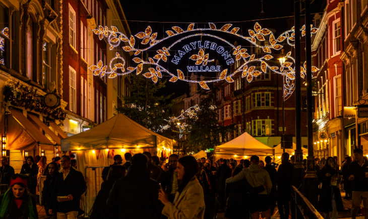 London Christmas lights 2025: An illuminated 'Marylebone Village' sign above a street full of people
