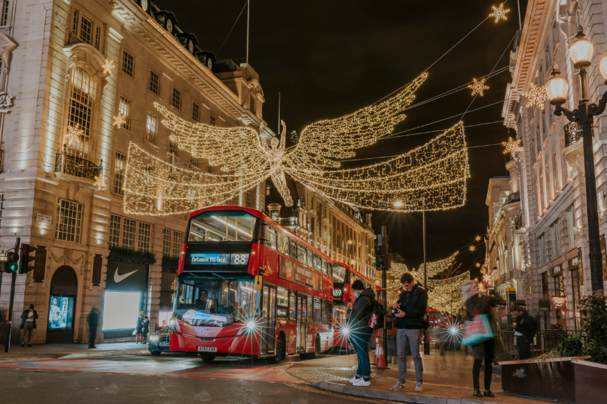 Regent Street London Christmas lights 2025: Glowing angels above Regent Street, with pedestrians and buses beneath