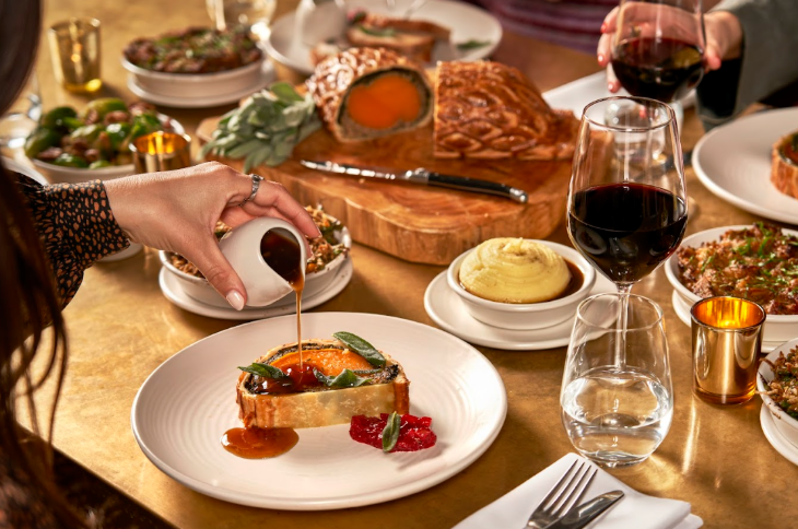 Thanksgiving 2025 in London: someone pouring gravy onto a plate of wellington, at a table covered in plates and wine glasses