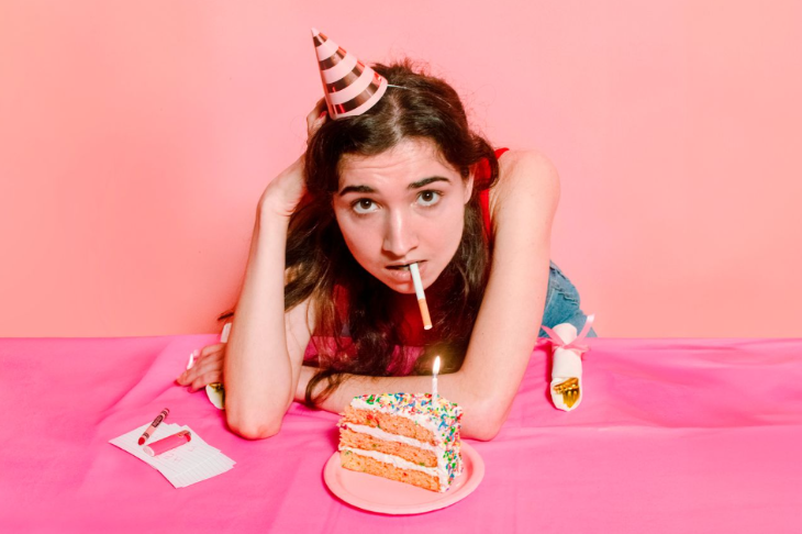 Today's events in London:  a woman wearing a party hat, leaning over a slice of birthday cake with a cigarette in her mouth