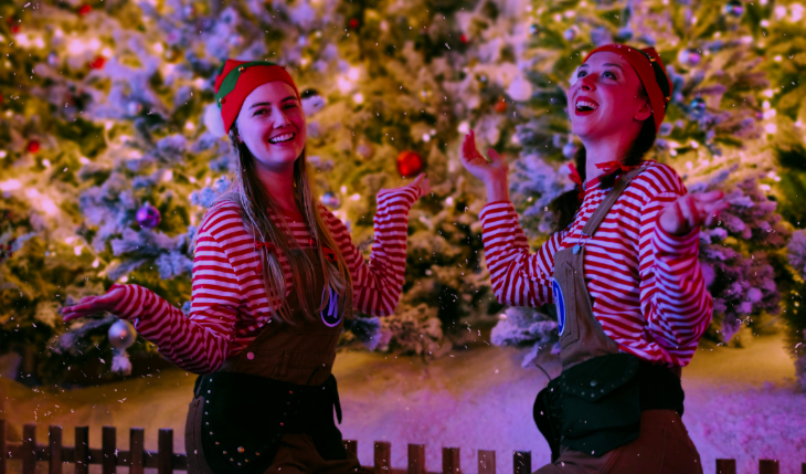 Things to do in London in November 2025: two people dressed as elves as snow falls in front of Christmas trees
