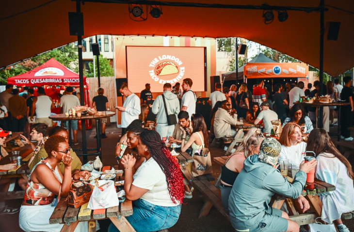 Things to do in London this weekend: people sitting at picnic benches eating and drinking, with food trader trucks in the background