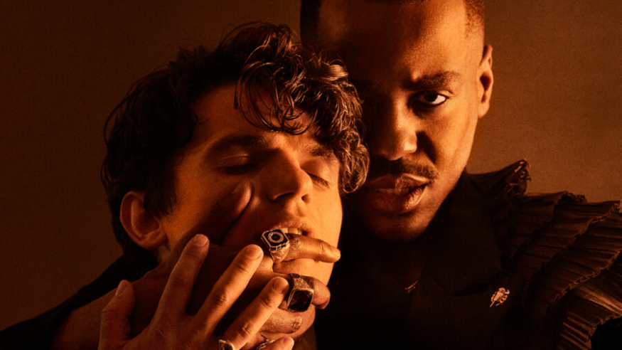 Things to do today in London: a close-up photo of one man holding his hand over another's mouth
