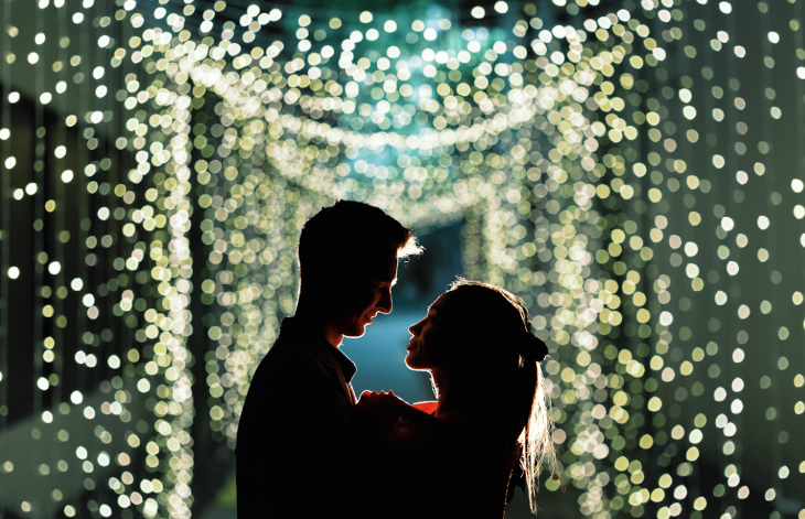 Christmas winter light festivals and trails London 2025: a couple illuminated against a backdrop of white-yellow fairy lights at the Vauxhall City Farm winter lights trail