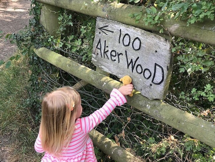 A small girl points to a 100 Aker Wood sign