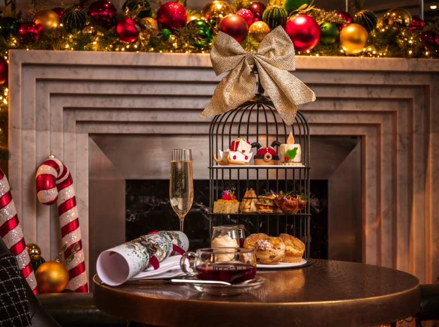 Best Christmas festive afternoon teas London 2025: a three-tiered stand topped with pastries resembling Santa, a sleigh and a candle, in front of a fireplace