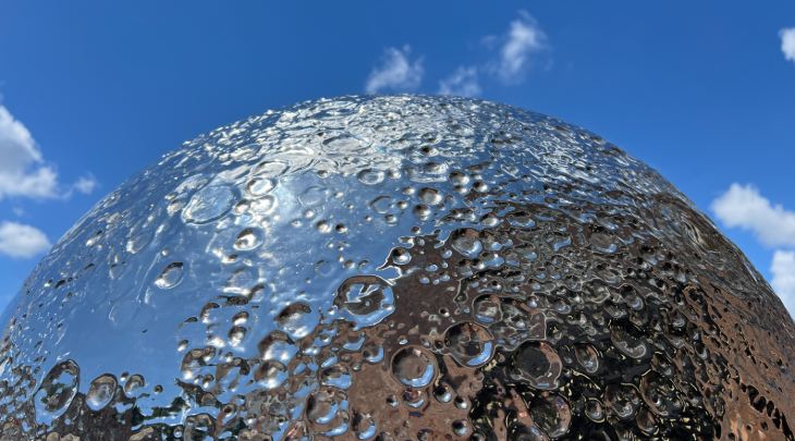 A replica of the Moon made from mirrored stainless steel, against the daytime sky
