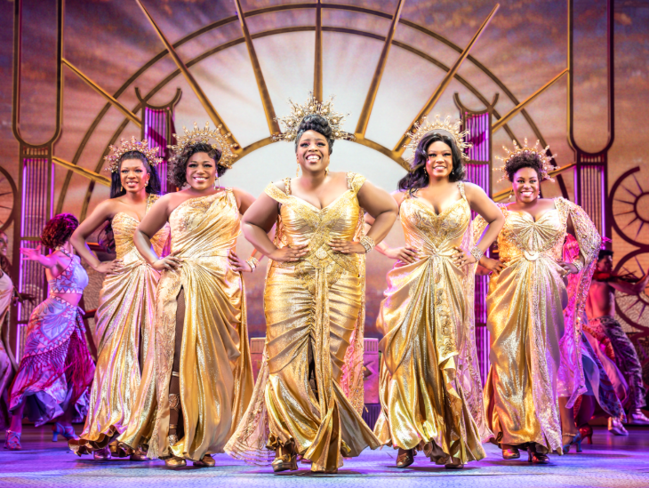 The Muses from Hercules, on stage in gold dresses