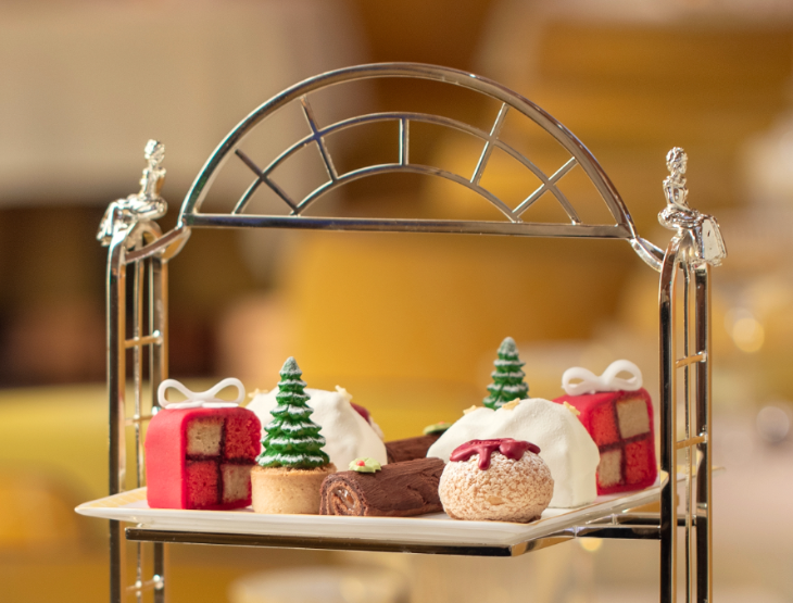 Best Christmas festive afternoon teas London 2025: the top tier of a cake stand containing battenberg designed to look like a gift, miniature Christmas trees, and other edible Christmas snacks