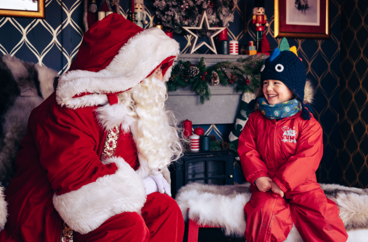 Things to do with kids in London at Christmas 2025: a young boy sitting talking to Santa in his grotto