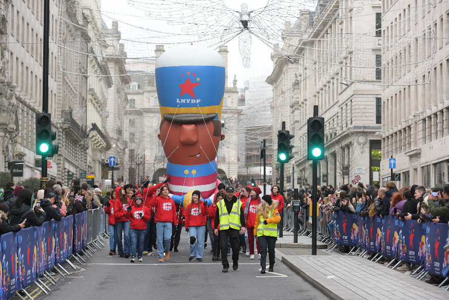London New Year's Day Parade 2026: People walking a giant balloon of a man in a marching band uniform through central London streets