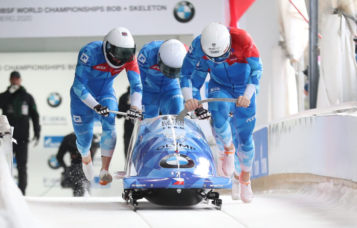 Winter sports in London: three members of a bobsleigh team in matching blue kit running beneath their sled and pushing it