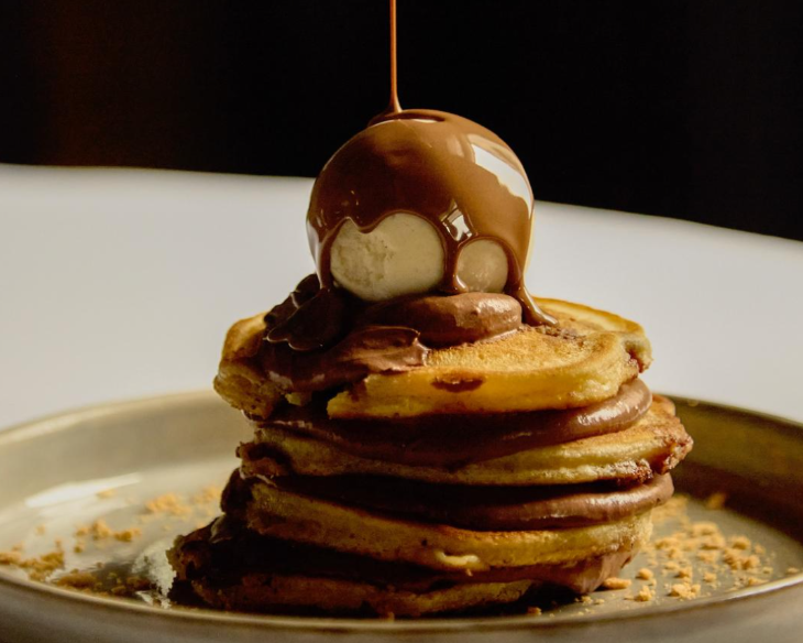 Pancake Day London 2026: melted chocolate being drizzled onto a ball of ice cream atop a stack of pancakes