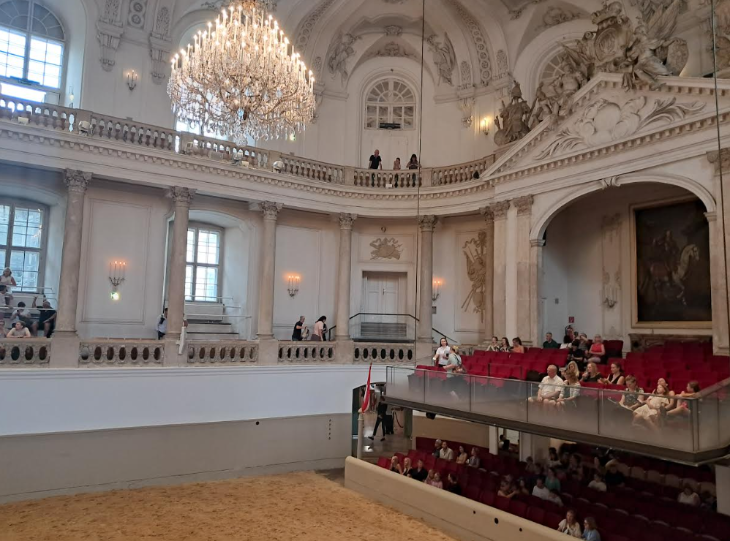 Best things to do in Vienna: people sitting in a theatre box beneath chandeliers overlooking a horse riding ring