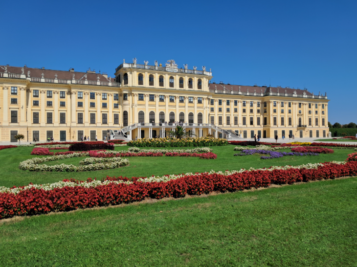 Best things to do in Vienna: the long front of a palace, with colourful flowerbeds in front