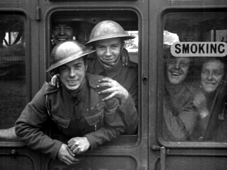 Things to do in London today: a black and white photo of soldiers leaning out a train window and smiling at the camera