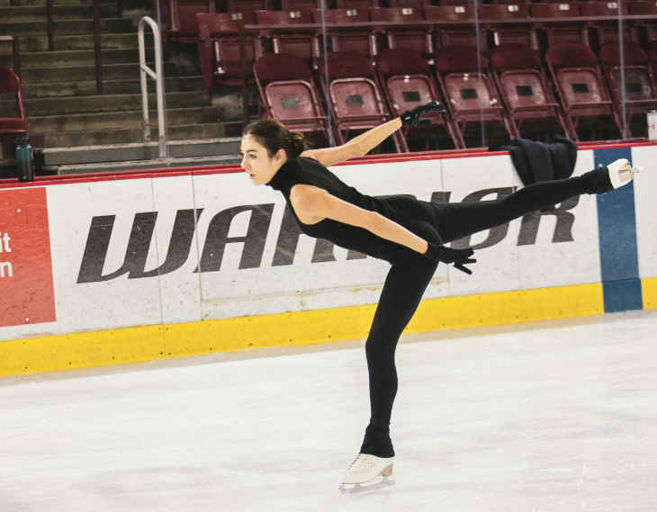 Winter sports in London: a figure skater dressed in black, balancing on one leg with the other leg stretched out behind her