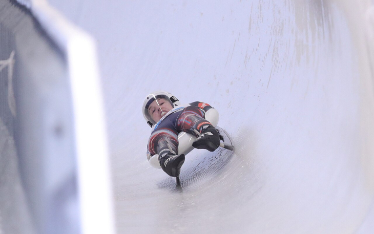 Winter sports in London:  a person lying flat on their back on a luge, hurtling feet first towards the camera