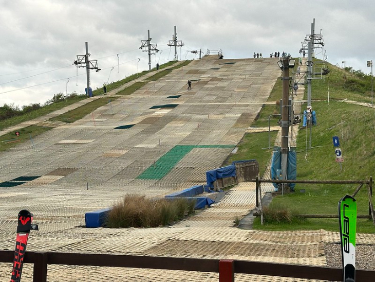 Winter sports in London:  an outdoor dry ski slope, surrounded by grass, beneath grey skies