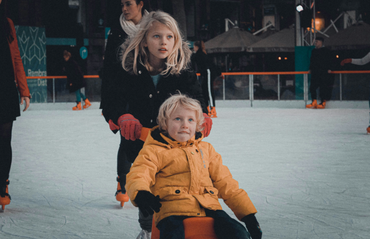 Permanent indoor ice rinks London: a girl pushing a younger boy on a ride-on skate aid on an ice rink