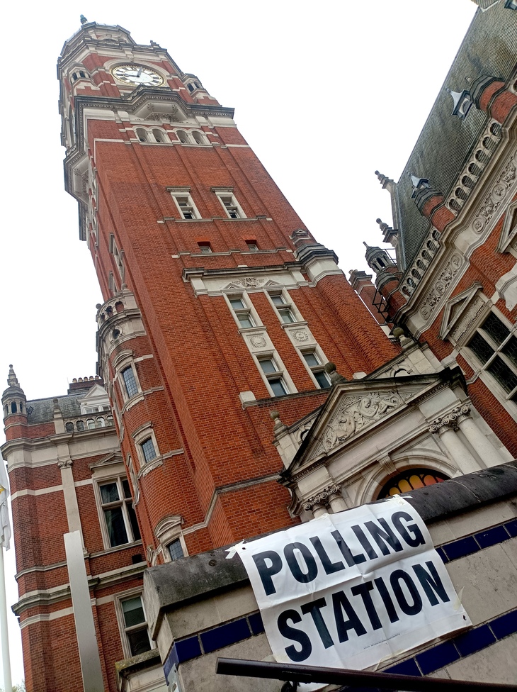 A polling station sign i front of a clocktower