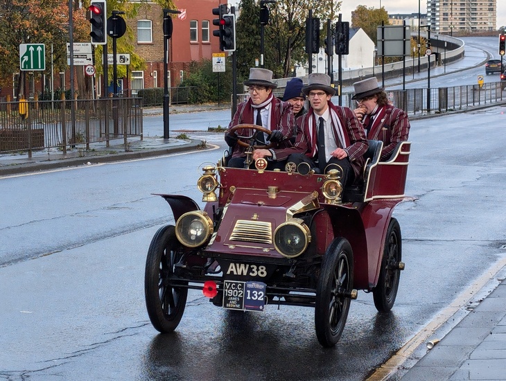 A vintage car loaded with guys in top hatsr