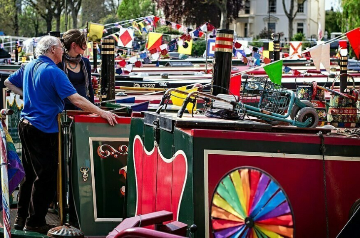 Canalway Cavalcade Little Venice 2026: two people standing on the deck of a canalboat, with bunting strung overhead