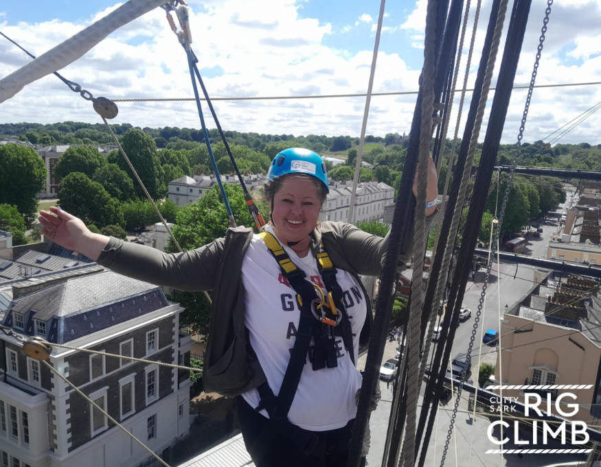 Daredevil activities London: a woman wearing a helmet, high above ground level, with one hand holding onto a rope and the other held out in a pose