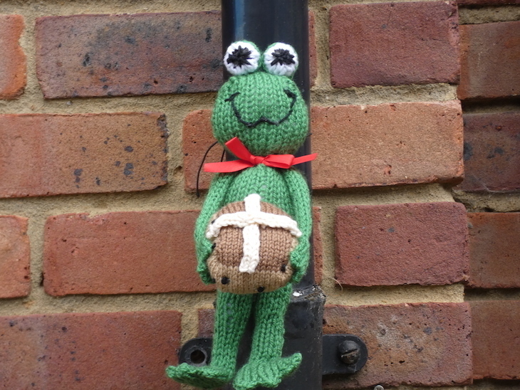 Frog Lane, Tunbridge Wells: a green knitted frog holding a hot cross bun, tied to a drainpipe