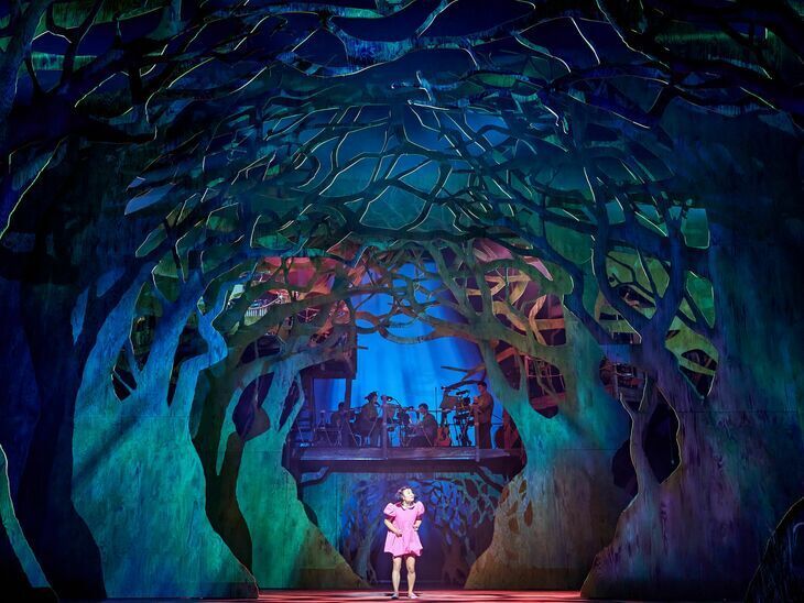 Family-friendly theatre shows London: a girl in a pink dress walking through a forest set on stage