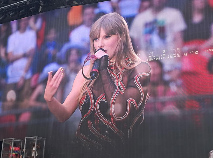 Taylor Swift's London: a photo of a large screen showing Taylor Swift holding a microphone and wearing the Reputation bodysuit: a black, one-sleeved bodysuit decorated with a red snake
